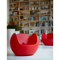 Fauteuil rouge dans un salon moderne, placé devant une grande bibliothèque remplie de livres et d’objets décoratifs.