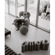 Photographie en noir et blanc d’un couple riant dans un fauteuil design, avec le banc “Amore” placé au premier plan