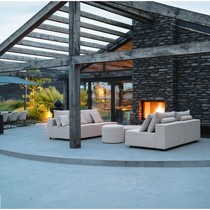 Deux canapés modulables Teton beige sous une pergola en bois, face à une cheminée, avec poufs ronds