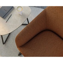 Détail de l'assise et de l'accoudoir du fauteuil Flux en tissu orange texturé, vu de dessus avec table d'appoint