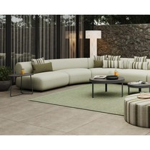 Canapé incurvé Onyx vert clair avec coussins rayés et unis, devant une table basse ronde et un tapis vert
