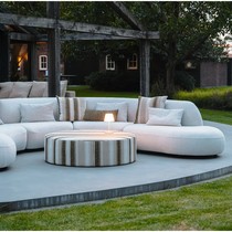 Canapé arrondi Onyx blanc cassé sur une terrasse ronde, autour d'un pouf rayé, sous un ciel du soir