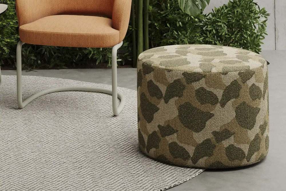 Pouf extérieur rond Peak à motif kaki posé sur un tapis, devant un fauteuil